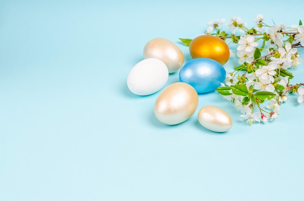 Oeufs de nacre peints de Pâques avec des fleurs de cerisier sur fond bleu avec espace de copie. Concept de saisonnalité, printemps, carte postale, vacances. Mise à plat, place pour le texte. Fermer