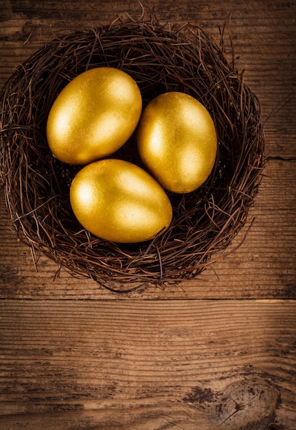 Photo oeufs d'or dans le nid sur fond de bois avec copie de texte