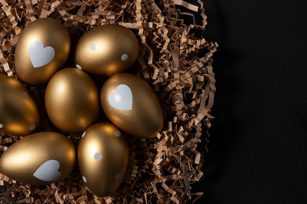 Photo des œufs d'or dans un nid de papier sur une table sombre