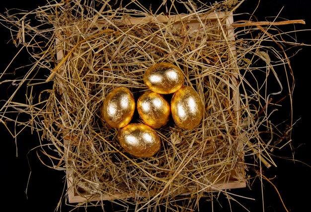 Photo oeufs d'or dans un nid sur la vue de dessus de la surface noire. concept de pâques.