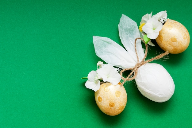 Oeufs d'or avec fleurs et lapin abstrait sur une surface verte