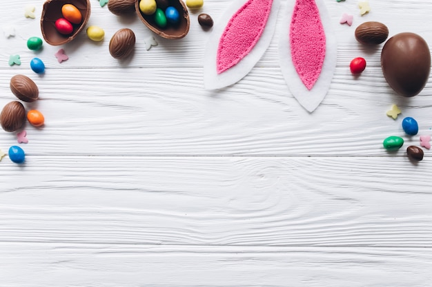 Oeufs de Pâques au chocolat et oreilles de lapin sur un fond en bois blanc.