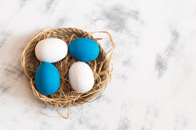 Les oeufs de Pâques blancs et bleus se trouvent sur un plateau fait de ficelle sous eux est du foin