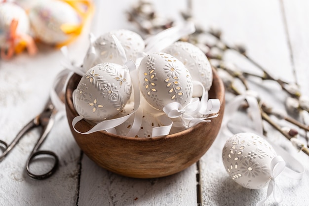 Oeufs de pâques blancs faits à la main avec des chatons de saule dans un bol en bois sur une table en bois.