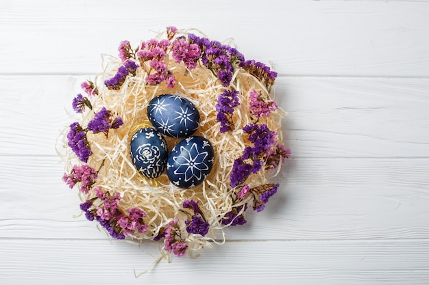 Oeufs de Pâques bleu foncé en nid sur fond en bois blanc