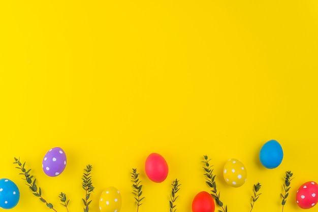 Oeufs de Pâques avec des branches de plantes sur la table jaune