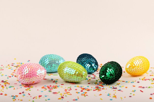 Oeufs de Pâques brillants colorés avec des paillettes. Garniture de pâtisserie vive sur fond pastel.