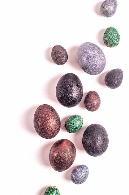 Oeufs de Pâques brillants en paillettes de couleurs différentes sur un fond blanc.