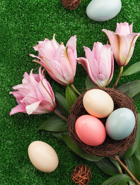 Oeufs de Pâques colorés dans le nid avec fleur de lys rose sur un fond d'herbe à gazon.