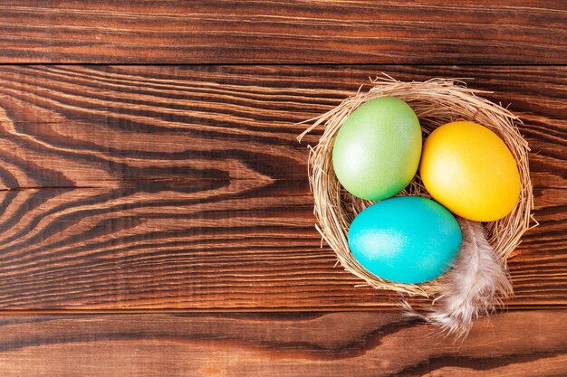 Oeufs de Pâques colorés dans le nid sur fond de bois, vue du dessus