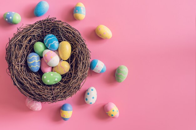 Oeufs de Pâques colorés dans un nid sur fond de couleur pastel rose avec espace.