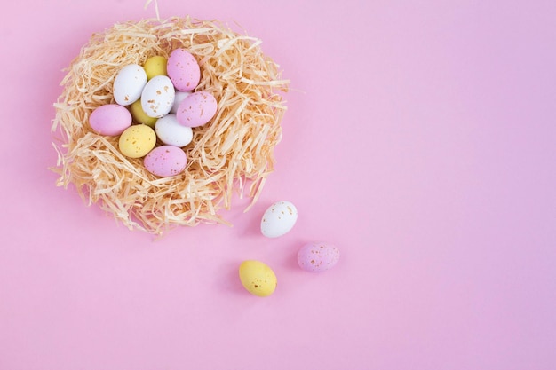 Oeufs de Pâques colorés dans un nid de paille sur fond rose Fond de vacances Espace de copie Vue de dessus