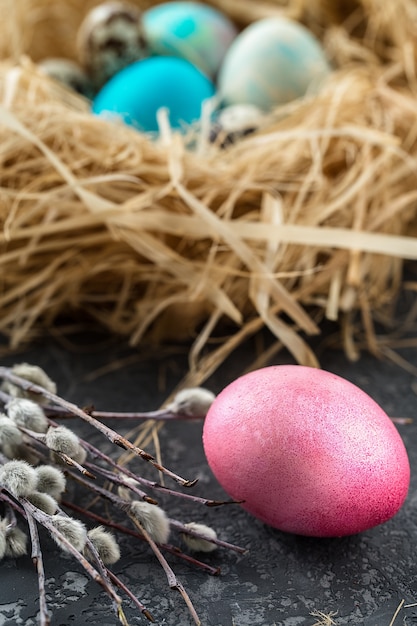 Oeufs de Pâques colorés dans un nid de paille sur une table grise