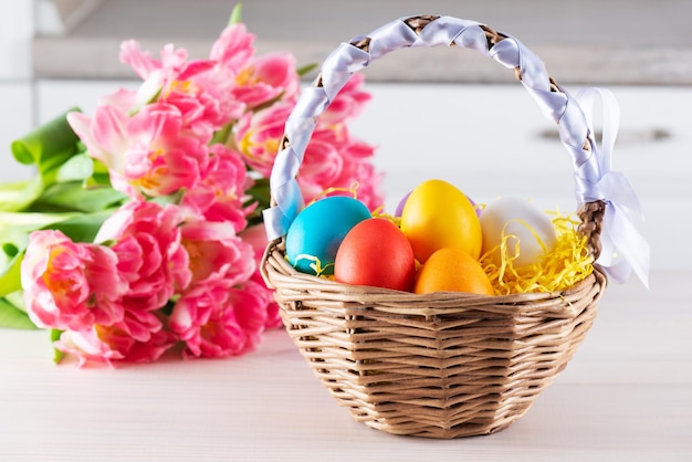 Oeufs de Pâques colorés dans un panier avec un bouquet de tulipes