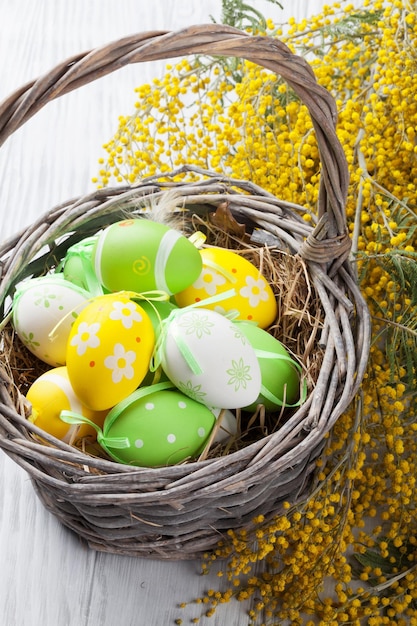 Oeufs de pâques colorés dans le panier et le mimosa