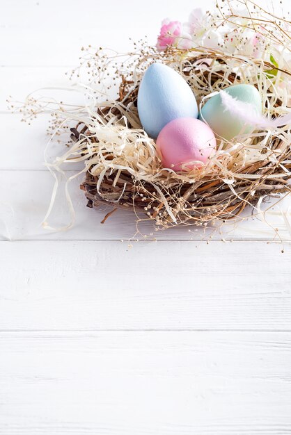 Oeufs de Pâques colorés dans un petit nid avec un fond en bois blanc, espace de copie. Événement de vacances