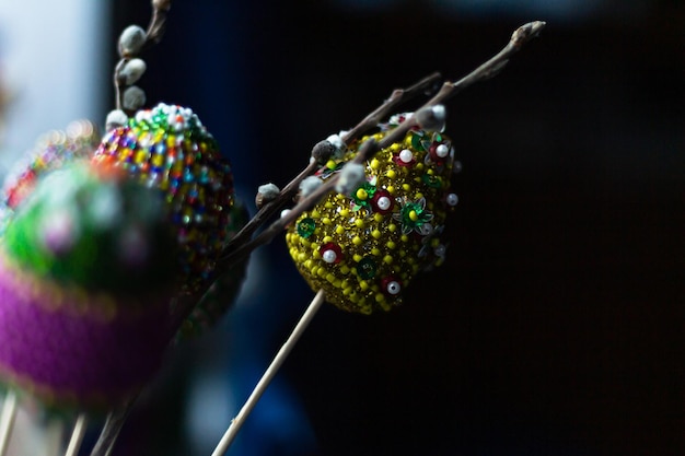 Oeufs de pâques colorés décorés de fils de couleurs vives et de perles avec une branche d'osier de saule