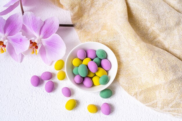 Oeufs de Pâques colorés et fleur d'orchidée phalaenopsis avec plaque sur un bureau blanc.