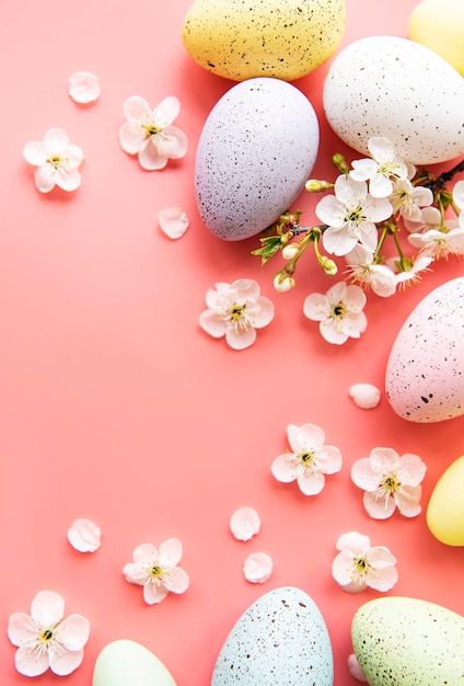 Oeufs de Pâques colorés avec des fleurs de printemps sur fond rose.