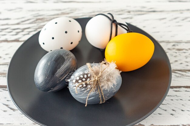 Oeufs de pâques colorés à la mode dans des couleurs sombres et des plumes sur une assiette sur une table en bois. Préparation des vacances de Pâques. Composition festive.