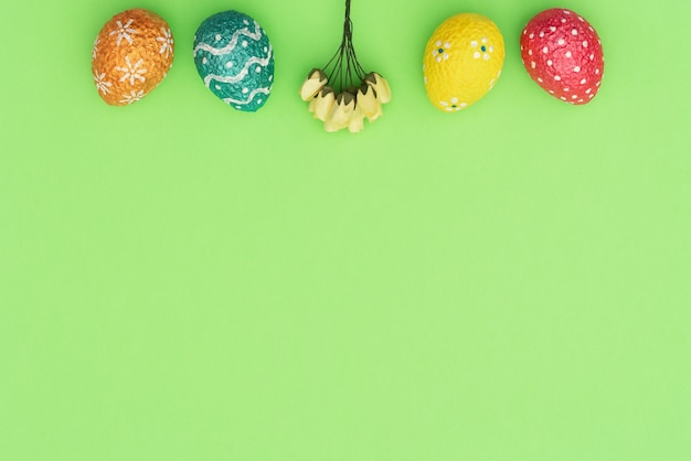 Oeufs de Pâques colorés peints en orange, bleu, rouge et jaune avec des fleurs de printemps jaune sur vert