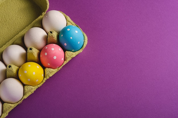 Oeufs de Pâques colorés à pois dans le bac à œufs sur fond uni violet violet, carte de voeux, espace copie, vue de dessus