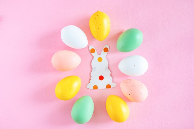 Oeufs de Pâques colorés et silhouettes de papier d'un lapin de Pâques sur fond rose