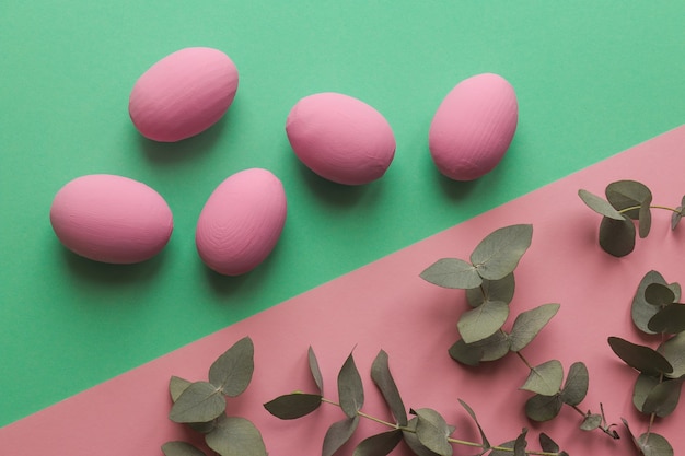 Oeufs de Pâques colorés sur table géométrique rose et vert avec des feuilles d'eucalyptus