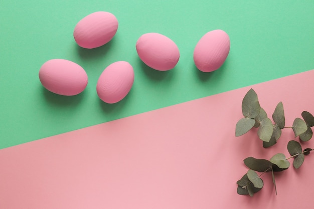 Oeufs de Pâques colorés sur texture rose et verte géométrique avec des feuilles d'eucalyptus