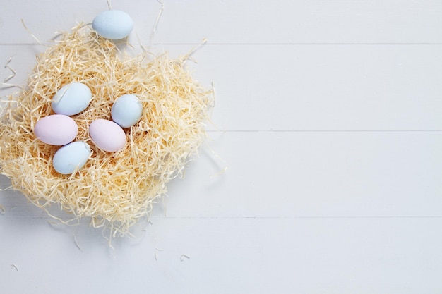 Oeufs de Pâques de couleur pastel bleu et rose dans un nid sur un fond en bois blanc. Vue de dessus, espace de copie