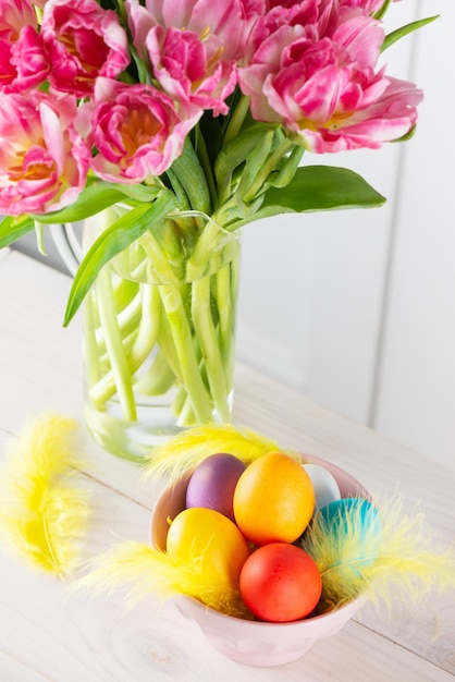 Oeufs de Pâques dans un bol avec des plumes et un bouquet de tulipes