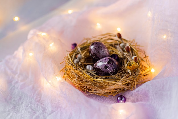 Oeufs de Pâques dans un nid et avec des fleurs sur le mur rose.