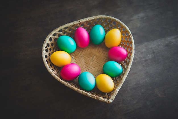 Oeufs de Pâques dans le panier sur fond de bois rustique. panier en paille sous forme de coeur avec des oeufs colorés peints pour les saintes vacances chrétiennes orthodoxes de Pâques.