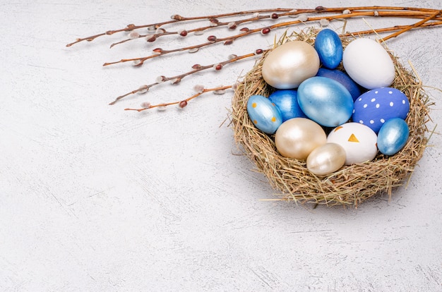 Oeufs de Pâques dans des tons bleus dans un nid de paille avec des branches de saule.