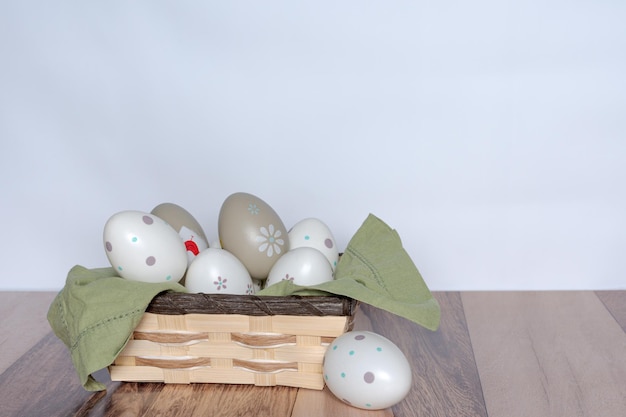 Oeufs de Pâques décorés dans un panier sur un fond en bois et un mur blanc