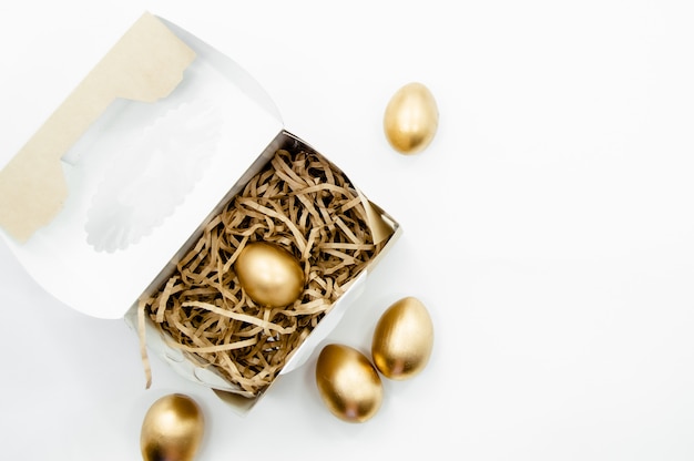 Oeufs de Pâques dorés dans une boîte avec des étoiles dorées sur fond blanc