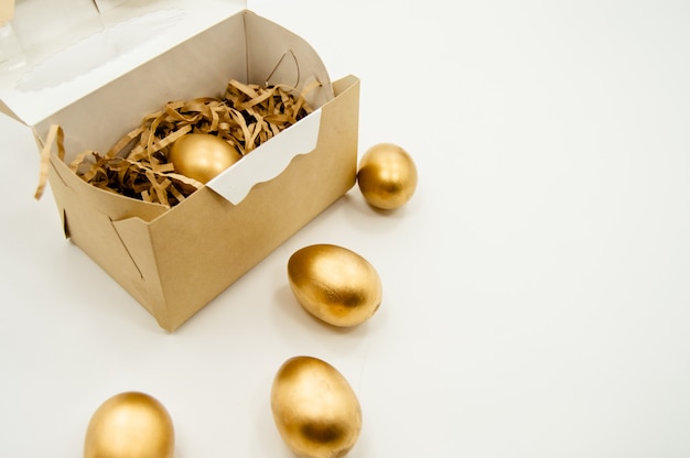 Oeufs de Pâques dorés dans une boîte avec des étoiles dorées sur fond blanc