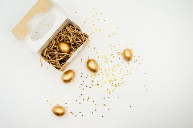 Oeufs de Pâques dorés dans une boîte avec des étoiles dorées sur fond blanc