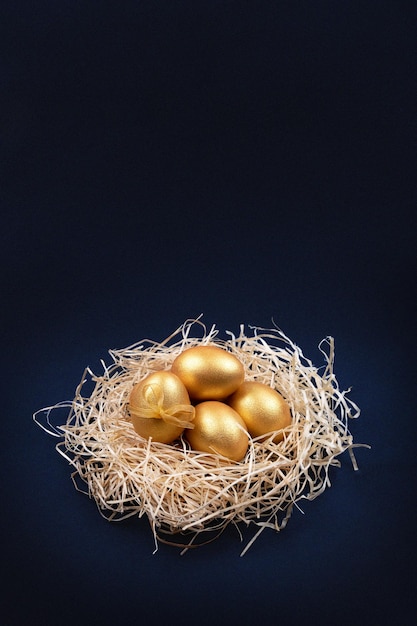 Photo des œufs de pâques dorés dans un nid décoratif sur un fond bleu foncé