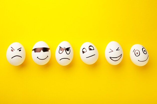 Oeufs de Pâques drôles avec différentes émotions sur son visage sur fond jaune.