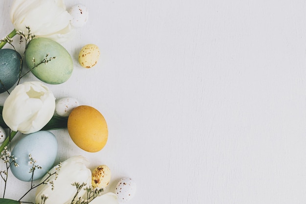 Des oeufs de Pâques élégants et des tulipes bordent un plat rustique en bois blanc avec un espace réservé au texte