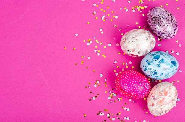 Oeufs de pâques faits à la main multicolores et confettis sur fond rose. Notion minimale. Vue d'en-haut. Espace pour le texte. Photo studio