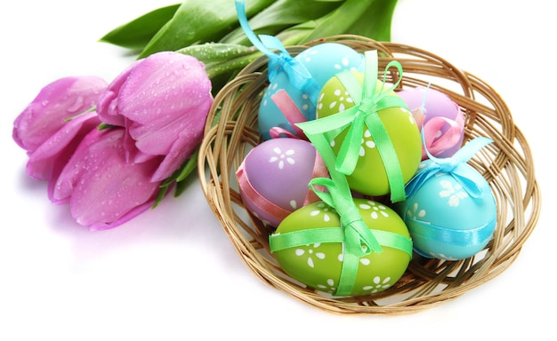 Oeufs de pâques lumineux dans le panier et tulipes isolés sur blanc