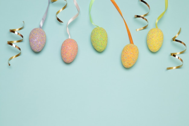 Oeufs de Pâques multicolores, bonbons dragées et bonbons d'or sur fond bleu, vue de dessus