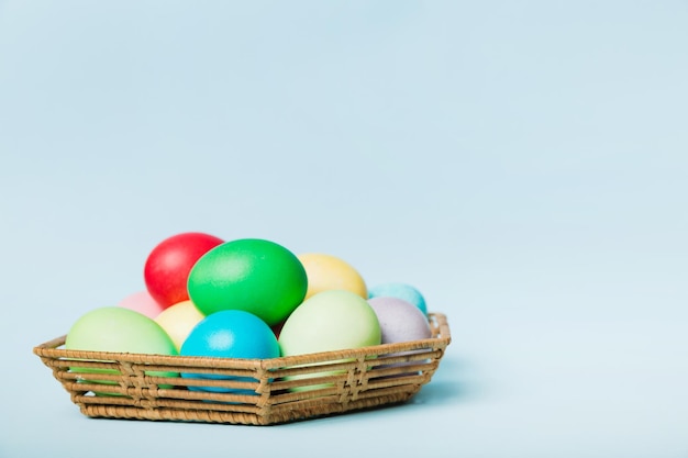 Oeufs de Pâques multicolores dans le panier tressé sur fond coloré Oeufs de Pâques de couleur pastel concept de vacances avec espace de copie