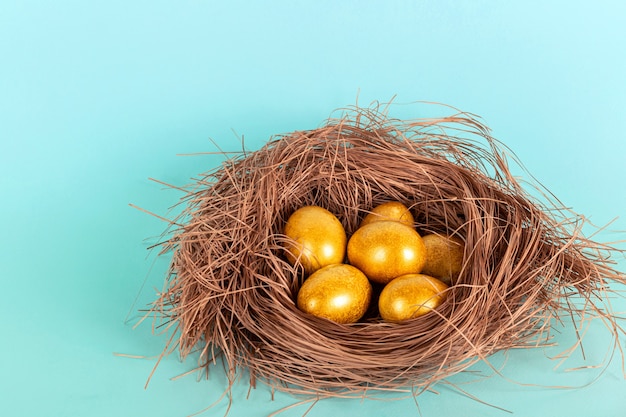 Oeufs de Pâques en or brillant dans un nid de paille sur fond bleu.