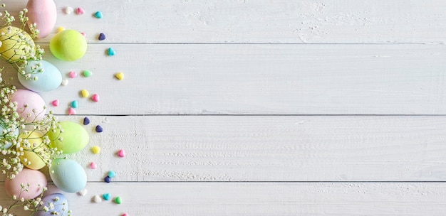 Oeufs de Pâques pastel colorés et petites fleurs sur table en bois blanc, espace copie, vue du dessus