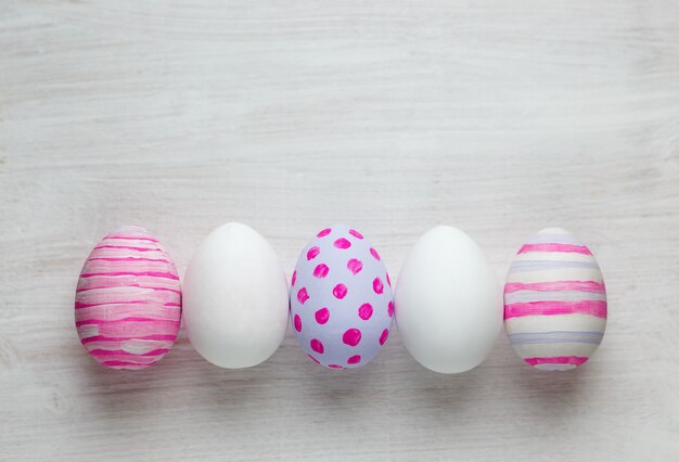 Oeufs de Pâques peints dans des couleurs pastel sur fond de bois blanc.