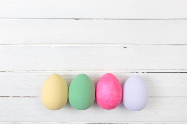 Oeufs de Pâques peints dans des couleurs pastel sur fond de bois blanc