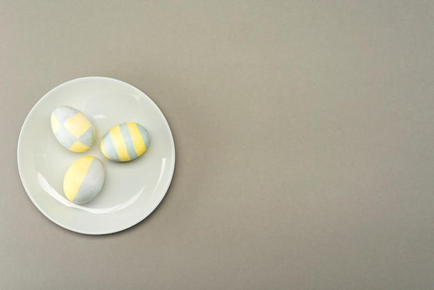 Oeufs de Pâques peints en jaune-gris dans une plaque grise sur une surface grise avec place pour le texte